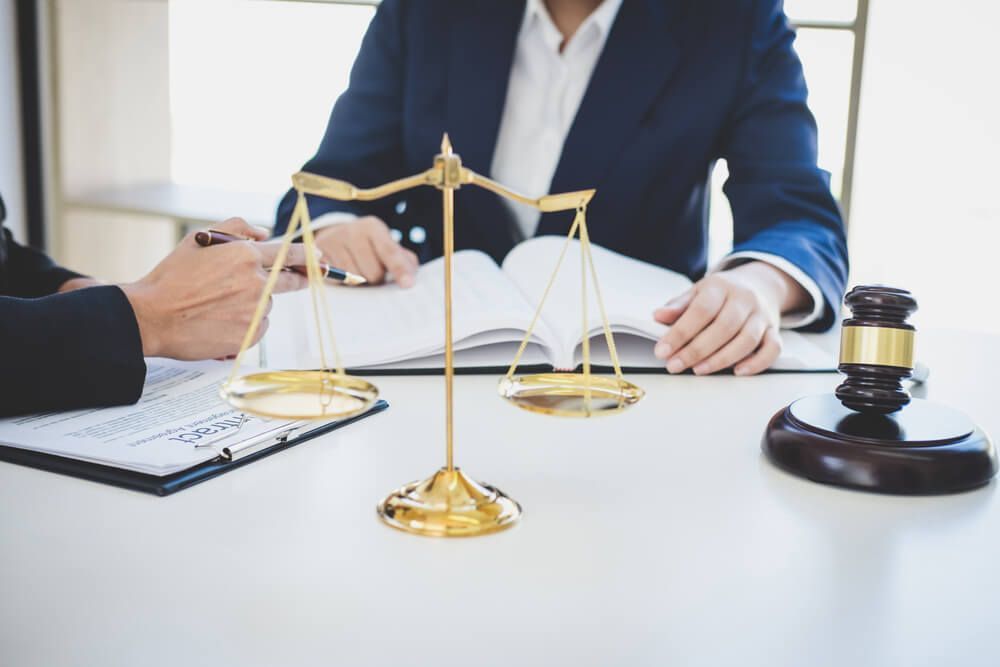 A woman is sitting at a table with a judge 's gavel and scales of justice.