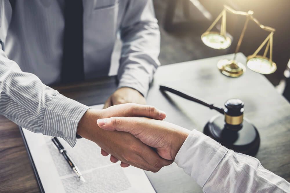 A lawyer is shaking hands with a client in front of a scale of justice.