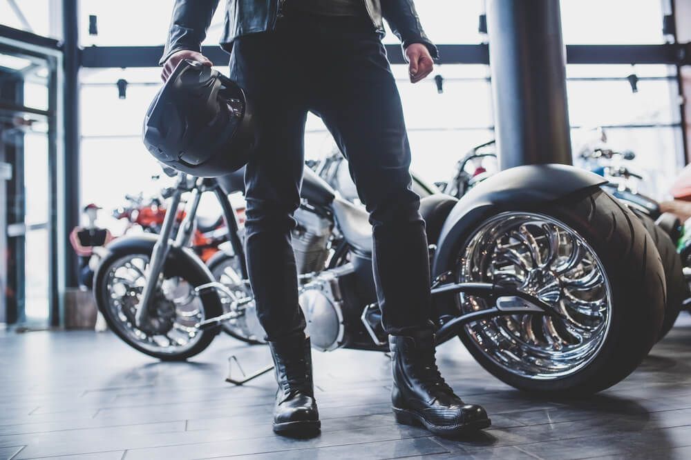 A man is standing next to a motorcycle in a showroom holding a helmet.