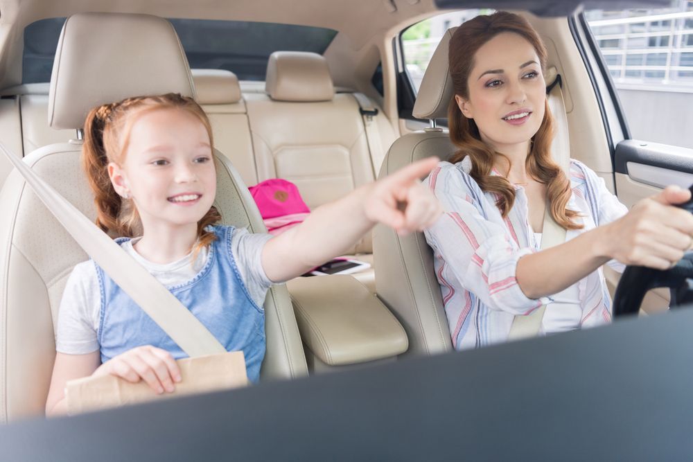 A woman is driving a car with a little girl in the back seat.