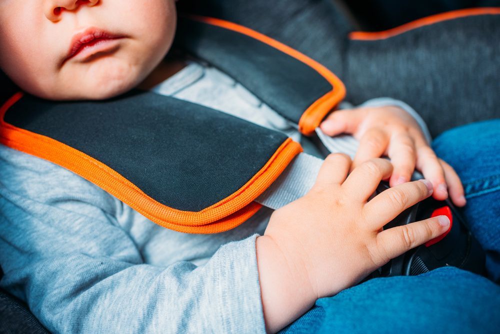 A baby is sitting in a car seat and adjusting his seat belt.