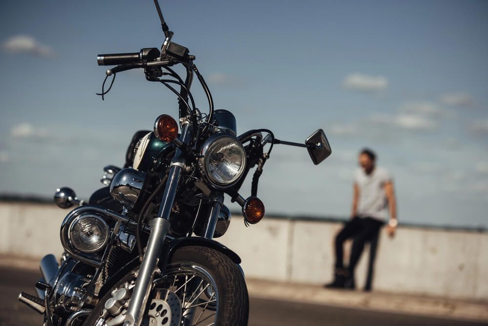 A man is sitting on a ledge next to a motorcycle.