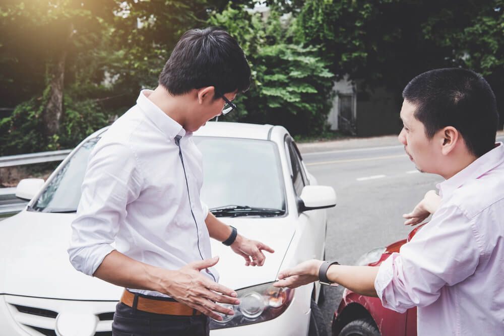 Two men are talking to each other in front of a car accident.