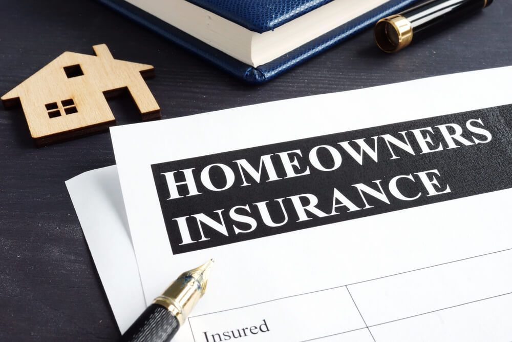 A homeowners insurance form with a pen and a wooden house on a table.