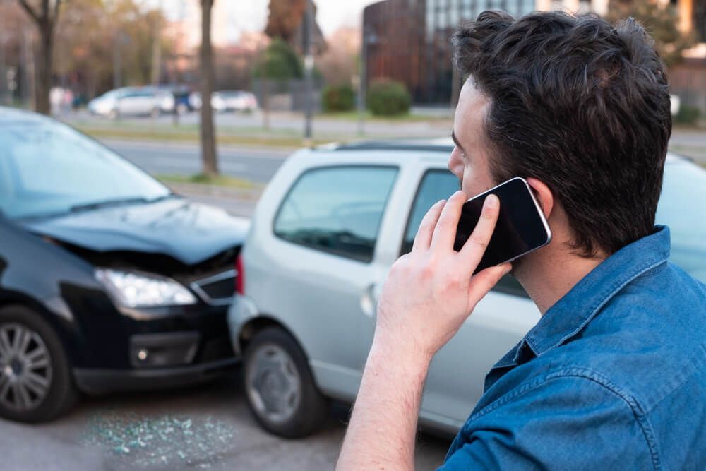A man is talking on a cell phone in front of a car accident.