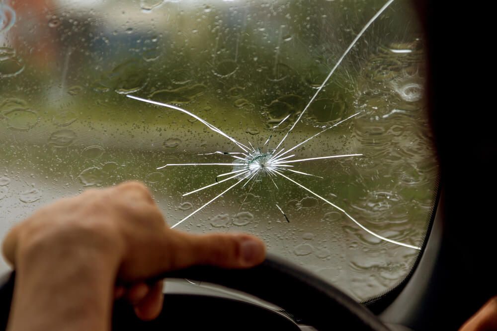 A person is pointing at a cracked windshield in a car.