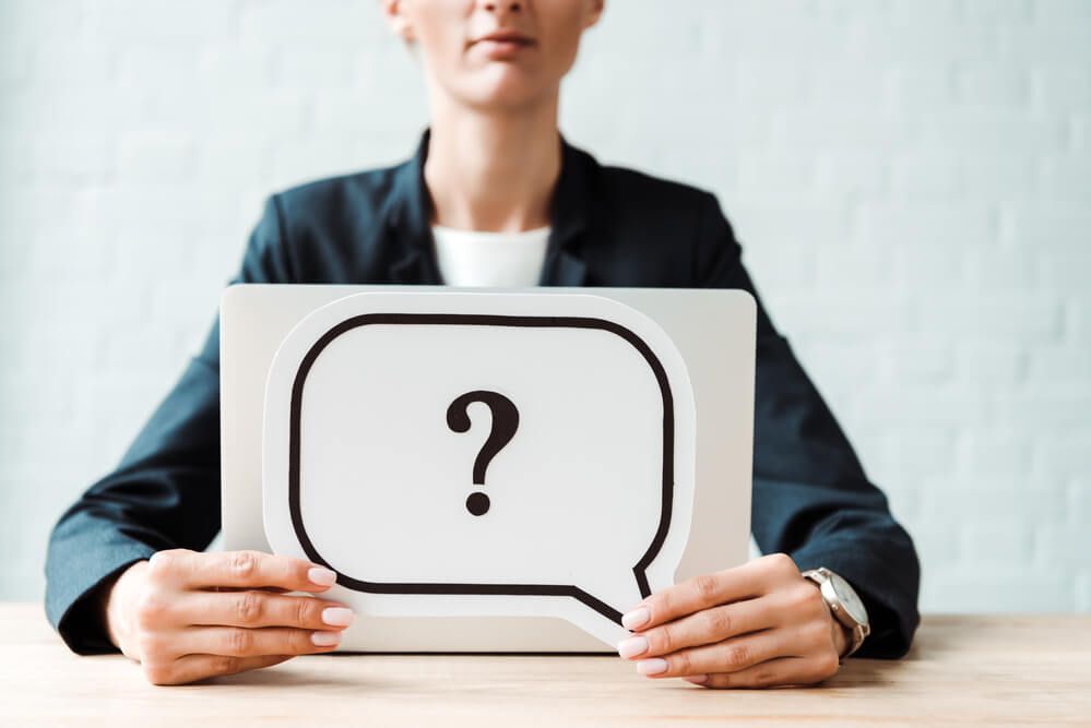 A woman is holding a sign with a question mark in a speech bubble.