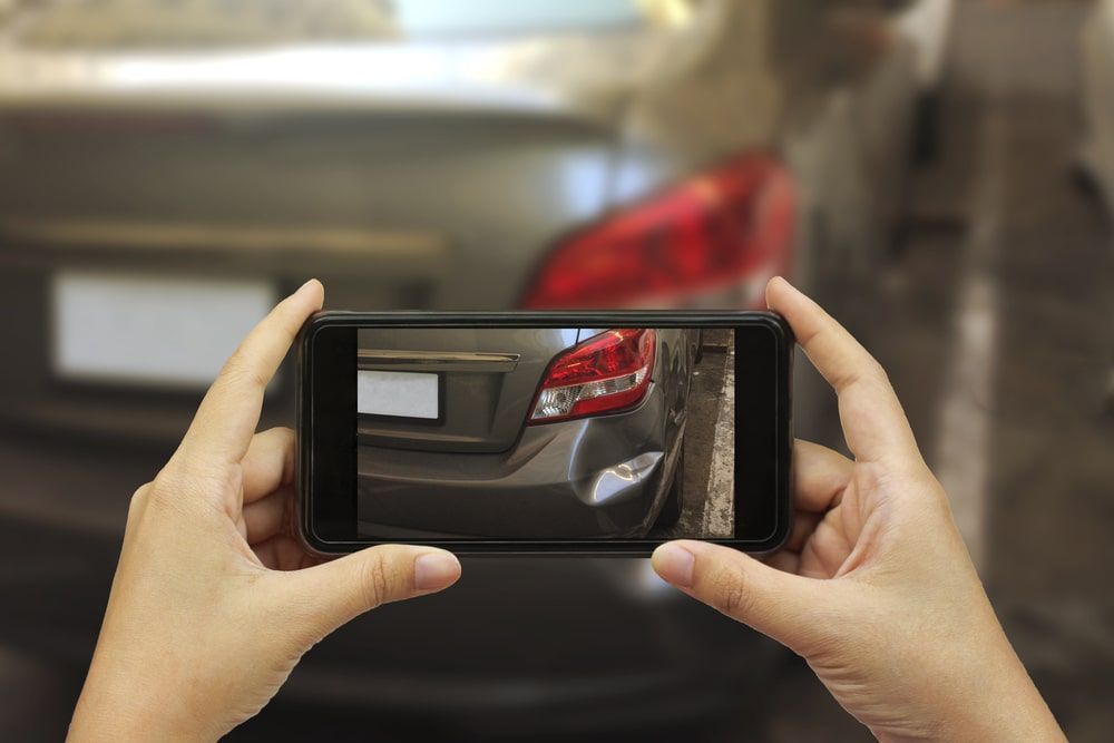 A person is taking a picture of a car with a cell phone.
