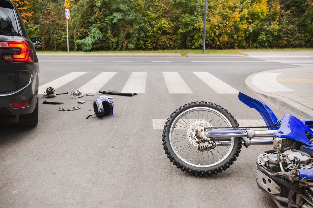 A motorcycle has crashed into a car on the side of the road.