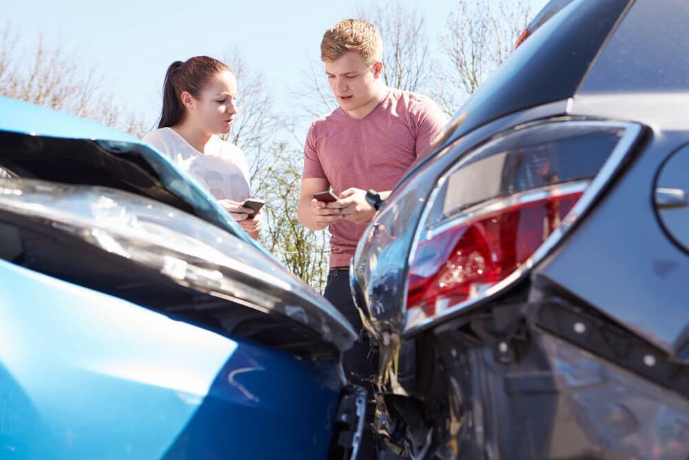 A man and a woman are looking at their phones after a car accident.