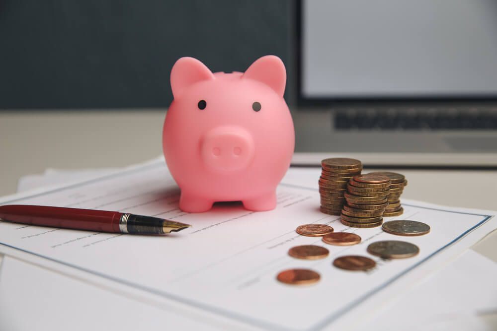 A pink piggy bank is sitting on top of a piece of paper next to stacks of coins and a pen.