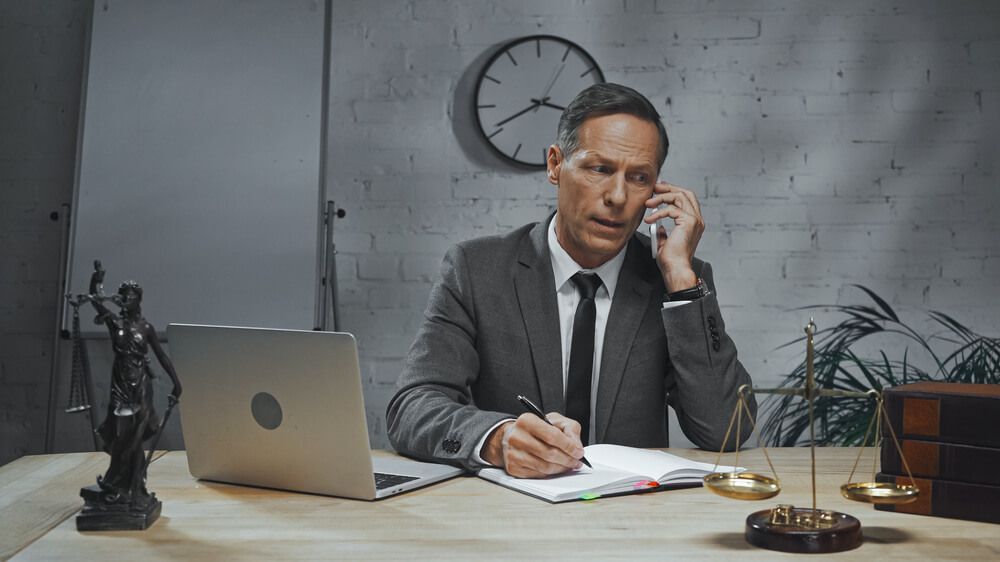 A lawyer is sitting at a desk talking on a cell phone.