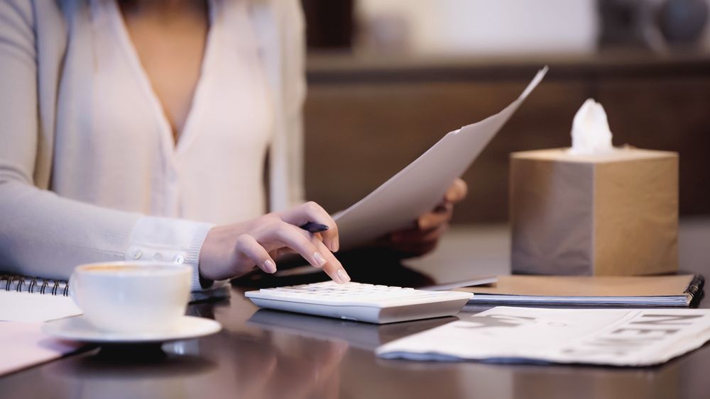 A woman is sitting at a desk with a cup of coffee and a calculator.