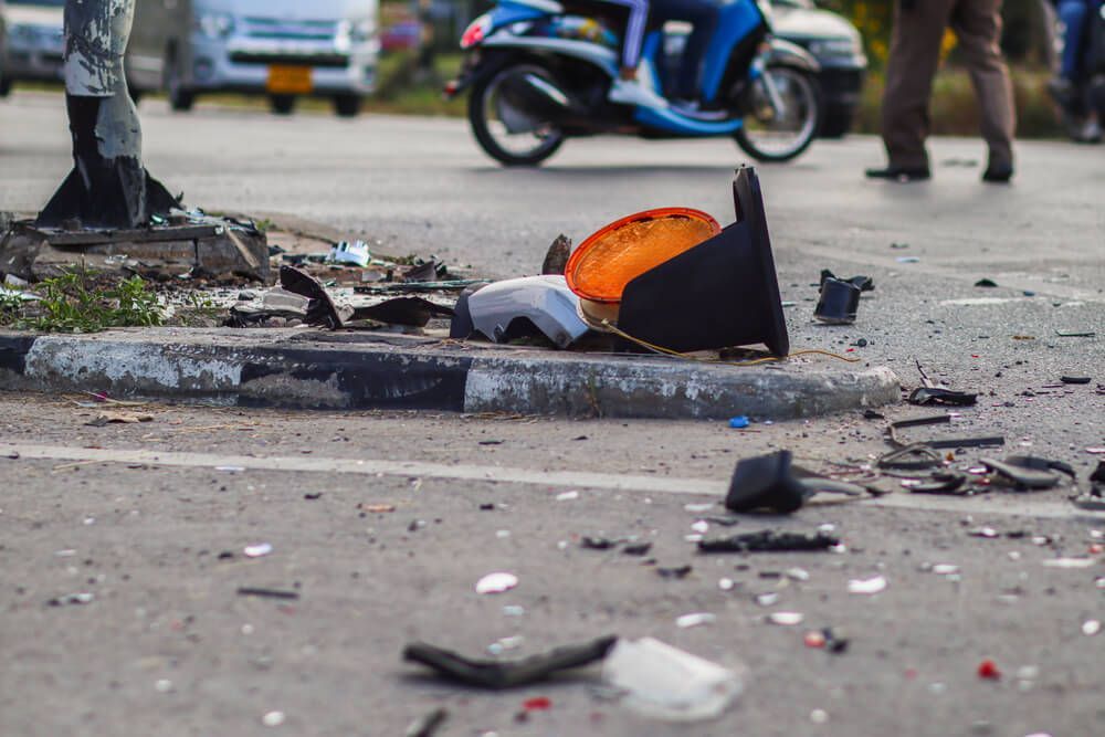 Debris and a detached orange motorcycle turn signal light lie on a roadside curb following a traffic accident.
