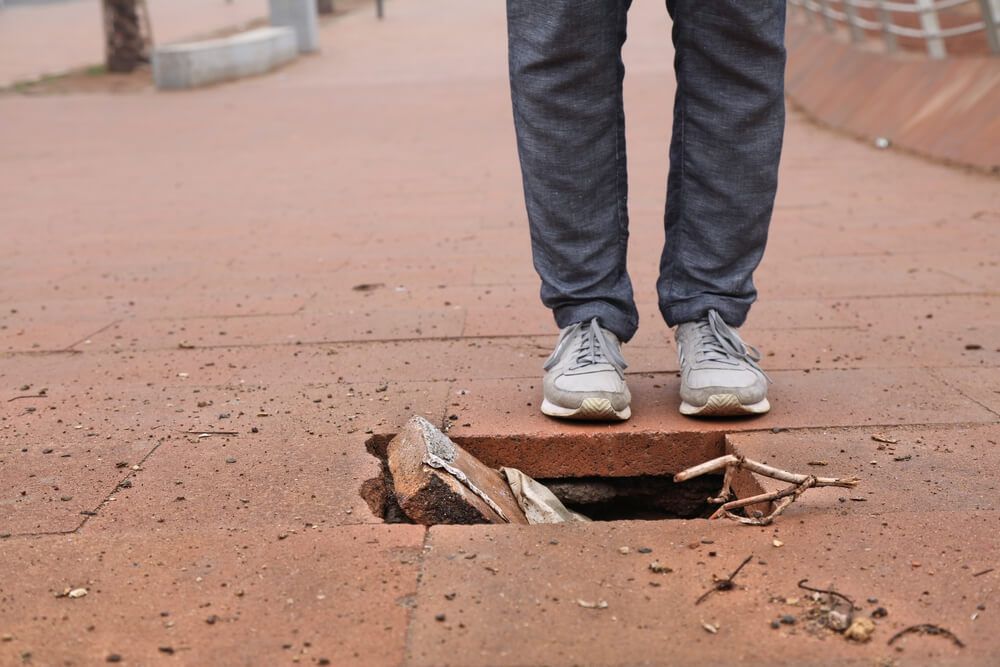 A person is standing in a manhole cover on a sidewalk.