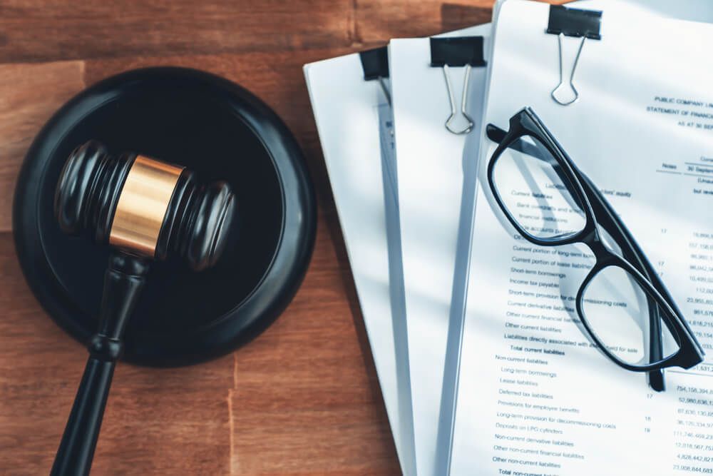A judge 's gavel , glasses and papers on a wooden table.