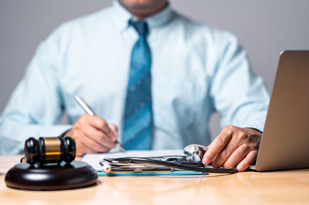 A man is sitting at a desk with a laptop and a stethoscope.
