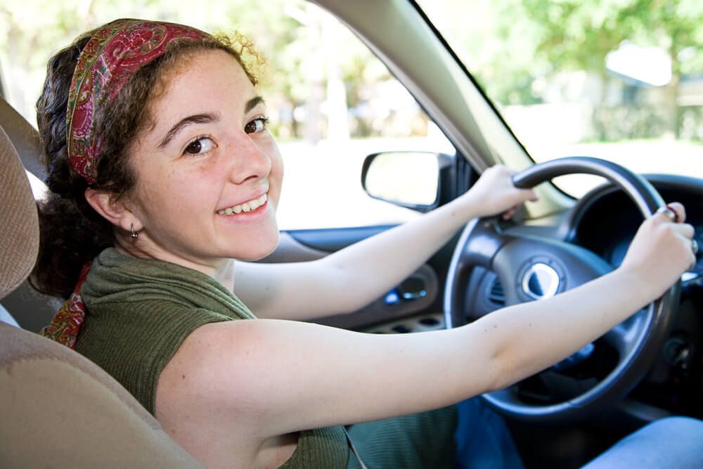 A young woman is smiling while driving a car