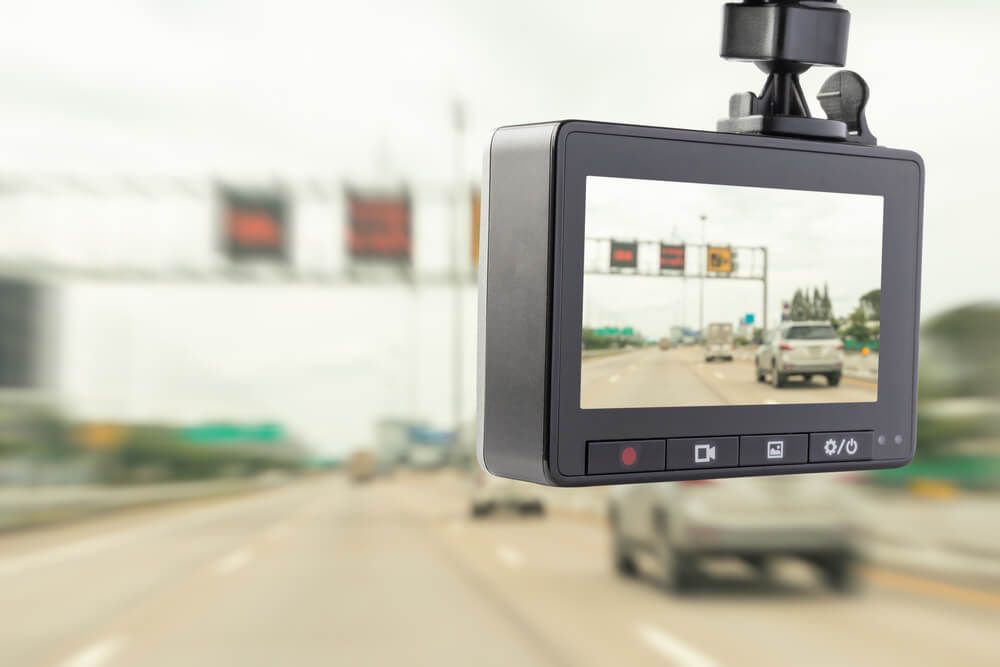 A dashcam mounted on a windshield, displaying a view of a highway with cars and overhead road signs.
