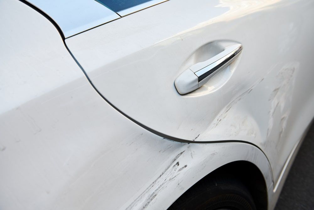 A close up of a white car with a damaged fender