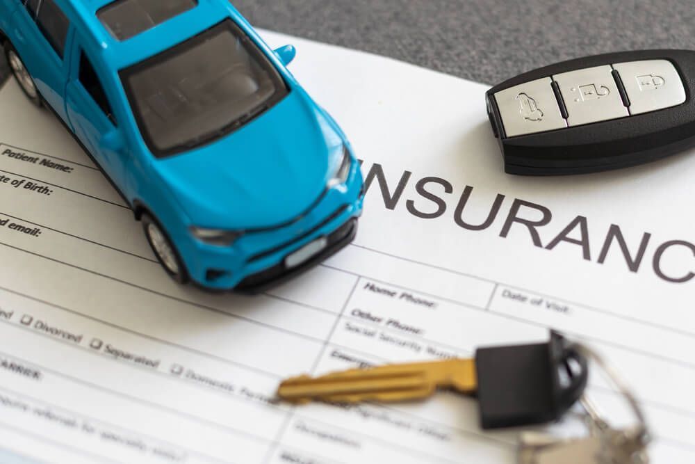 A blue toy car is sitting on top of a car insurance form.