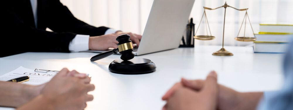 A judge is holding a gavel while sitting at a table with two people.