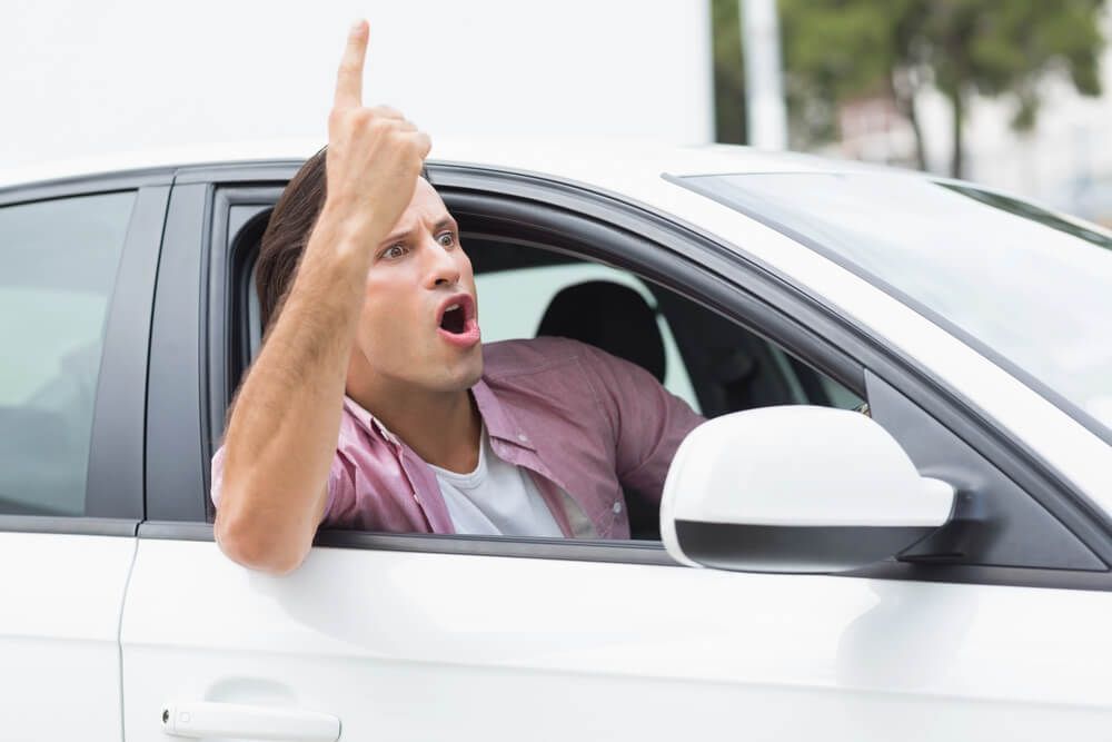 A man is driving a car and making a rude gesture.