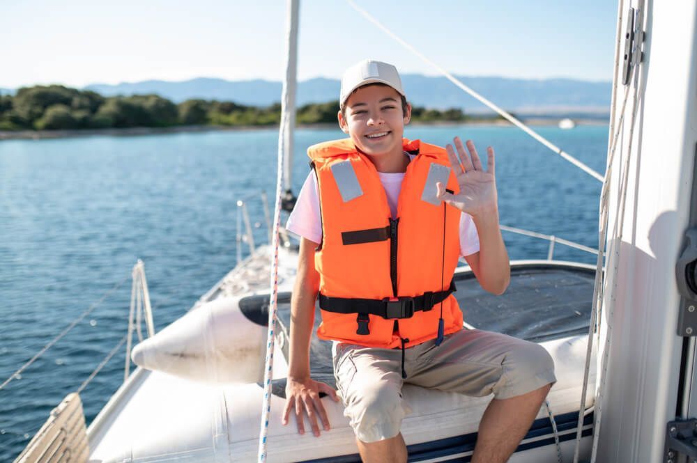 A young boy wearing an orange life jacket is sitting on a boat.