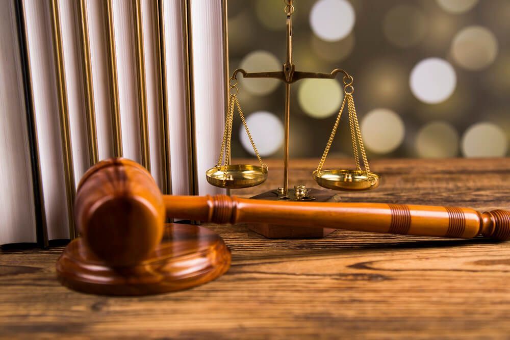A wooden gavel and scales of justice are on a wooden table.