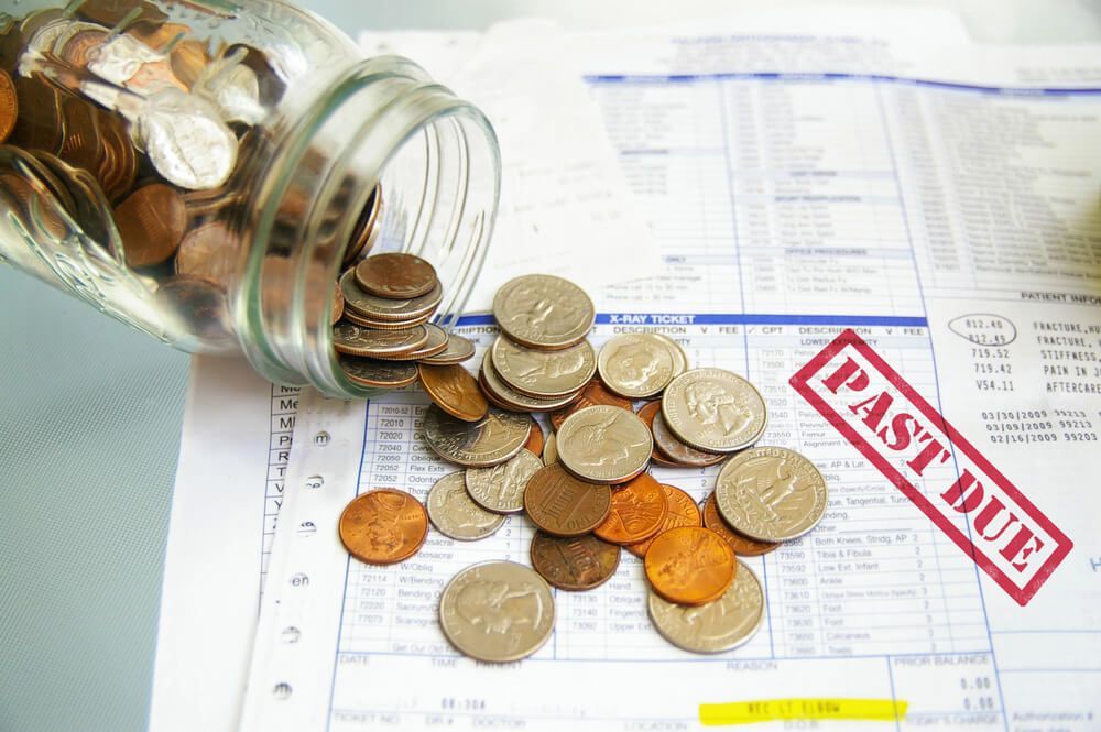 A clear glass jar tipped over spilling coins onto a stack of bills stamped with a red