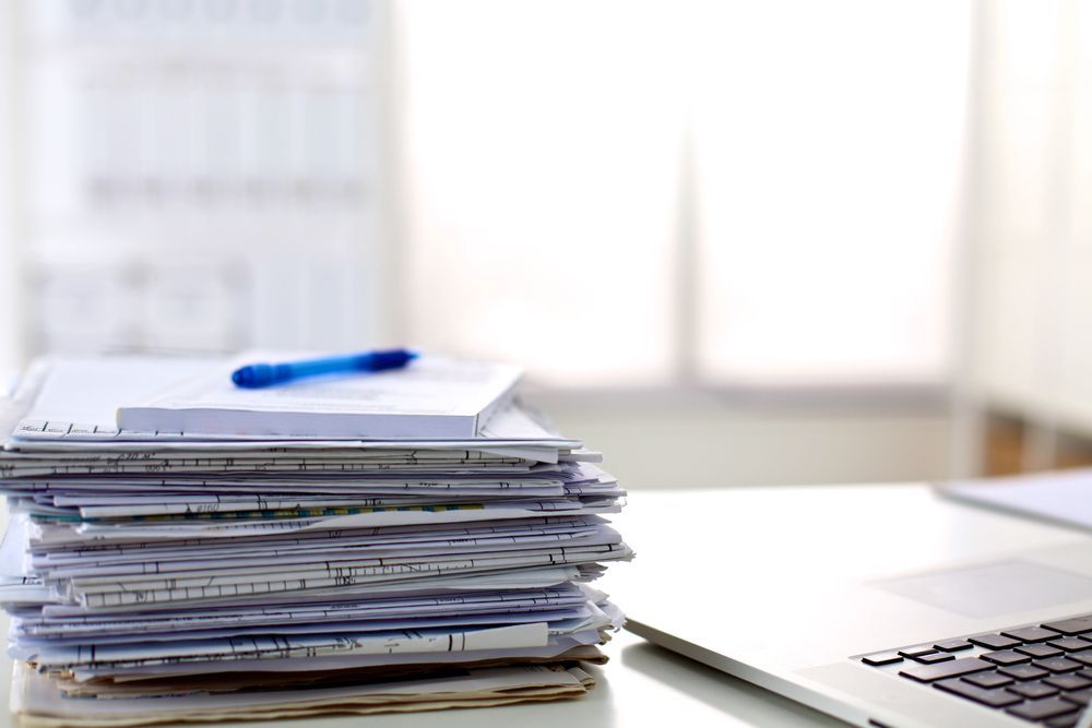 A stack of papers is sitting on a desk next to a laptop.