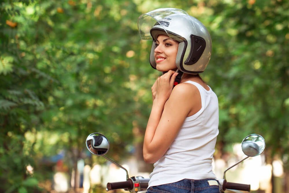 A woman wearing a helmet is sitting on a scooter.