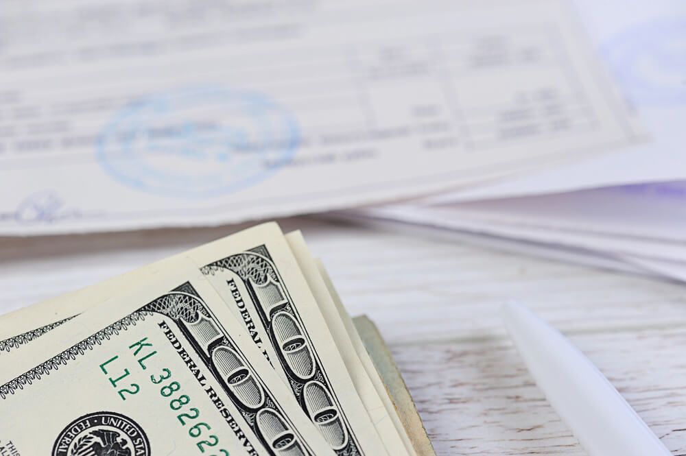 A stack of money is sitting on a table next to a pen and a check.