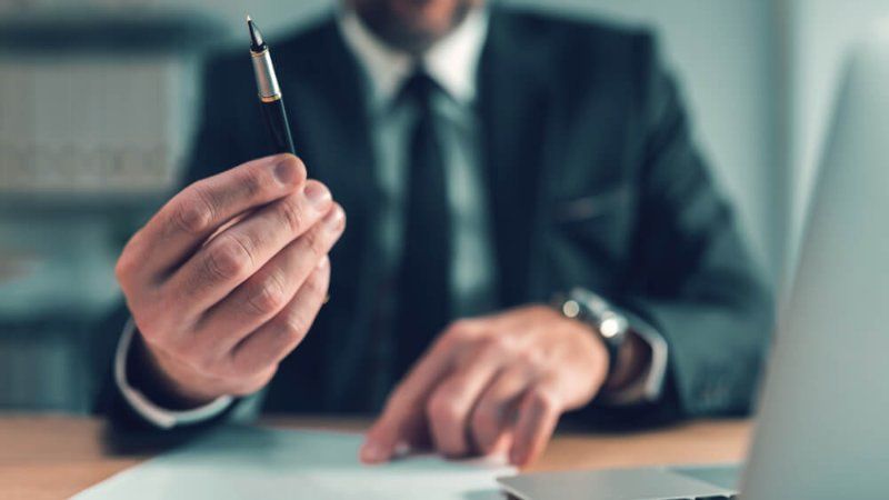 A man in a suit and tie is sitting at a desk holding a pen.