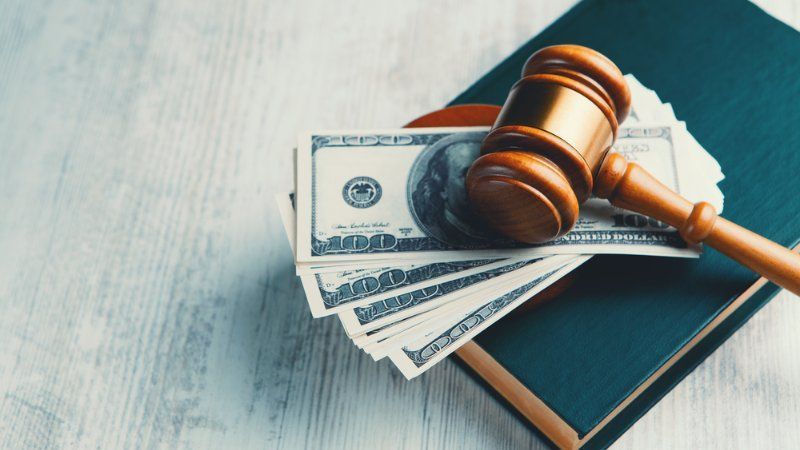 A wooden judge 's gavel is sitting on top of a pile of money on top of a book.