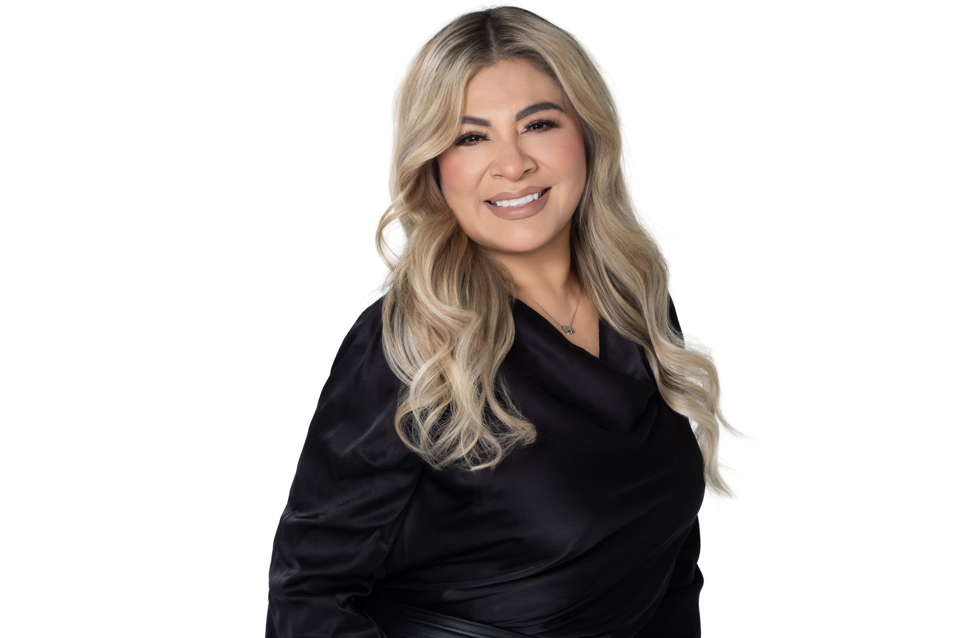 Smiling person with long blonde hair, wearing a black satin blouse, posing against a white background.