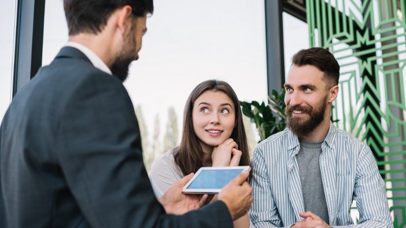 A man is talking to a woman and a man while holding a tablet.