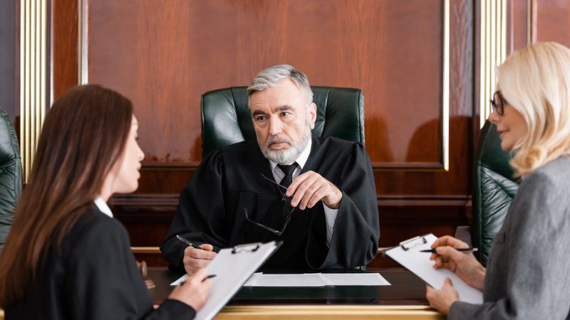 Two lawyers are sitting in front of a judge in a courtroom.