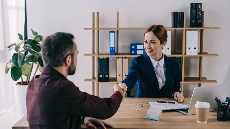 A man and a woman are shaking hands at a desk in an office.