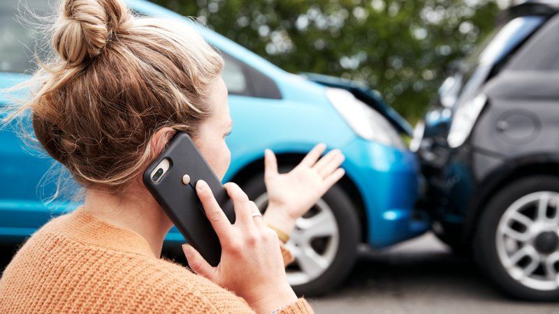 A woman is talking on a cell phone in front of a car accident.