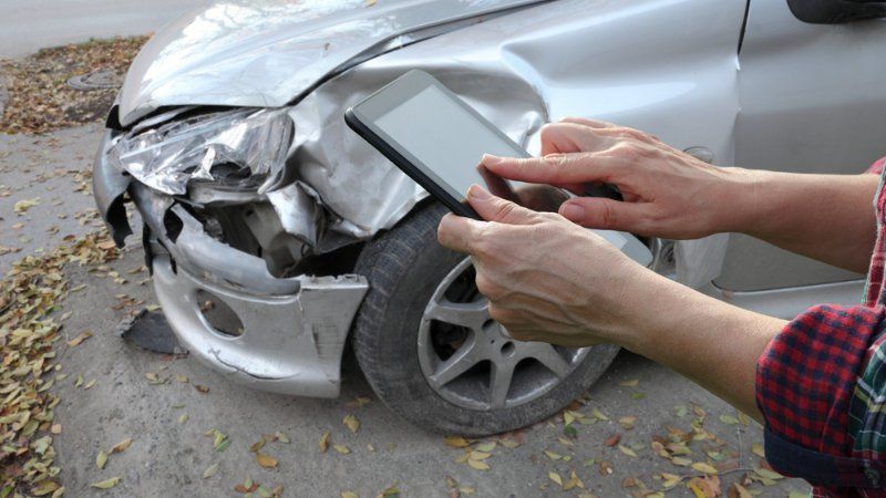 A person is taking a picture of a damaged car with a tablet.