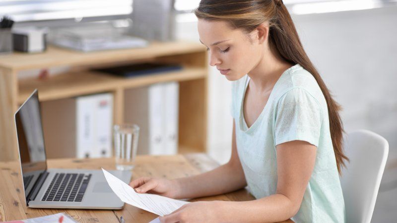 A woman is sitting at a desk with a laptop and a piece of paper.