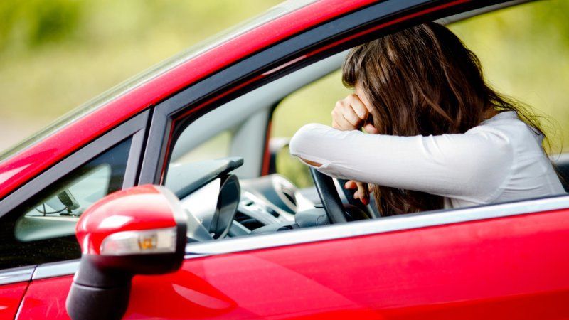 A woman is sitting in a red car with her head in her hand.