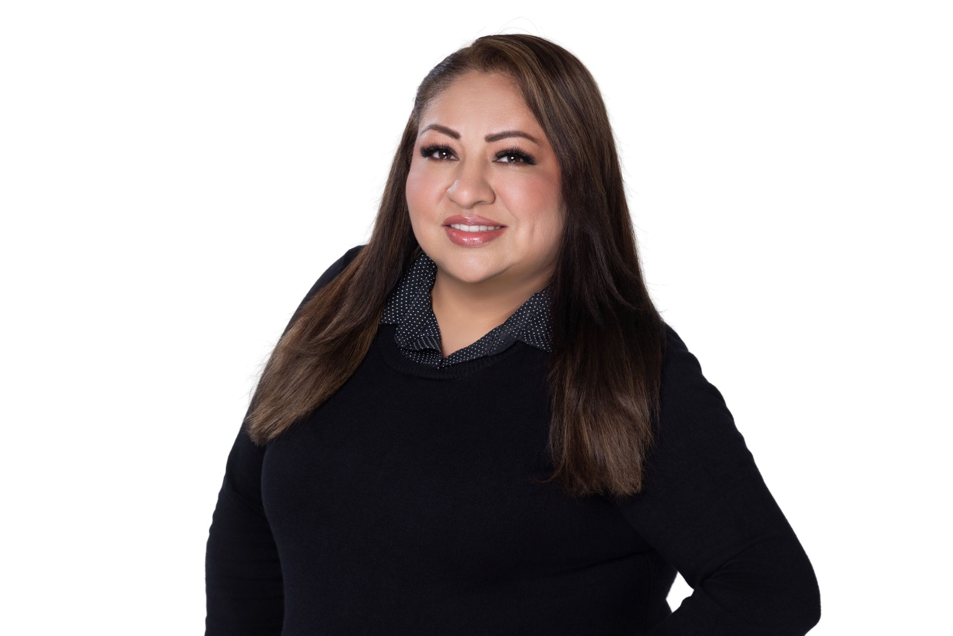 A person with long brown hair, wearing a black sweater over a dark collared shirt, smiling against a white background.