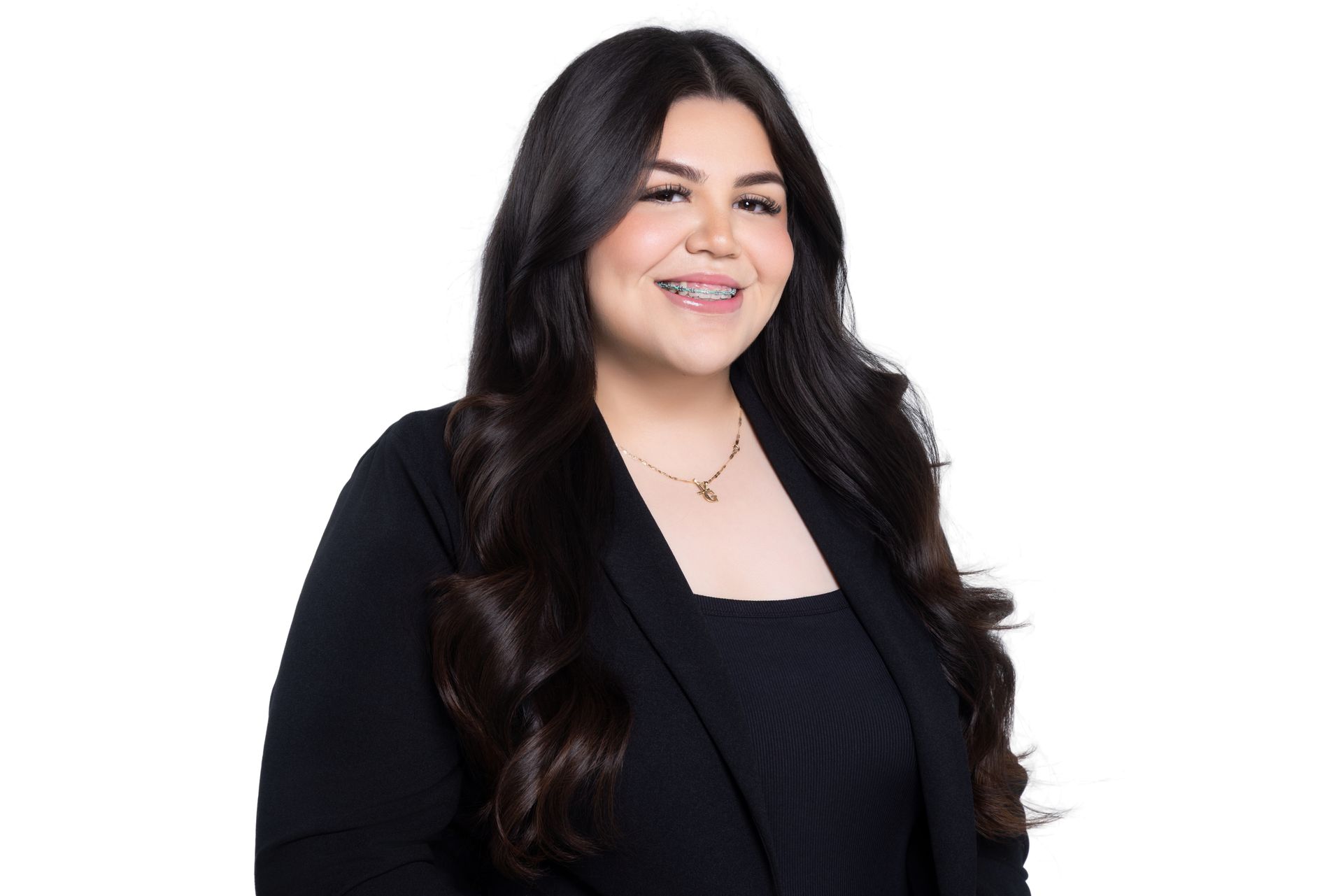A person with long, dark hair wearing a black blazer smiles warmly against a plain white background.