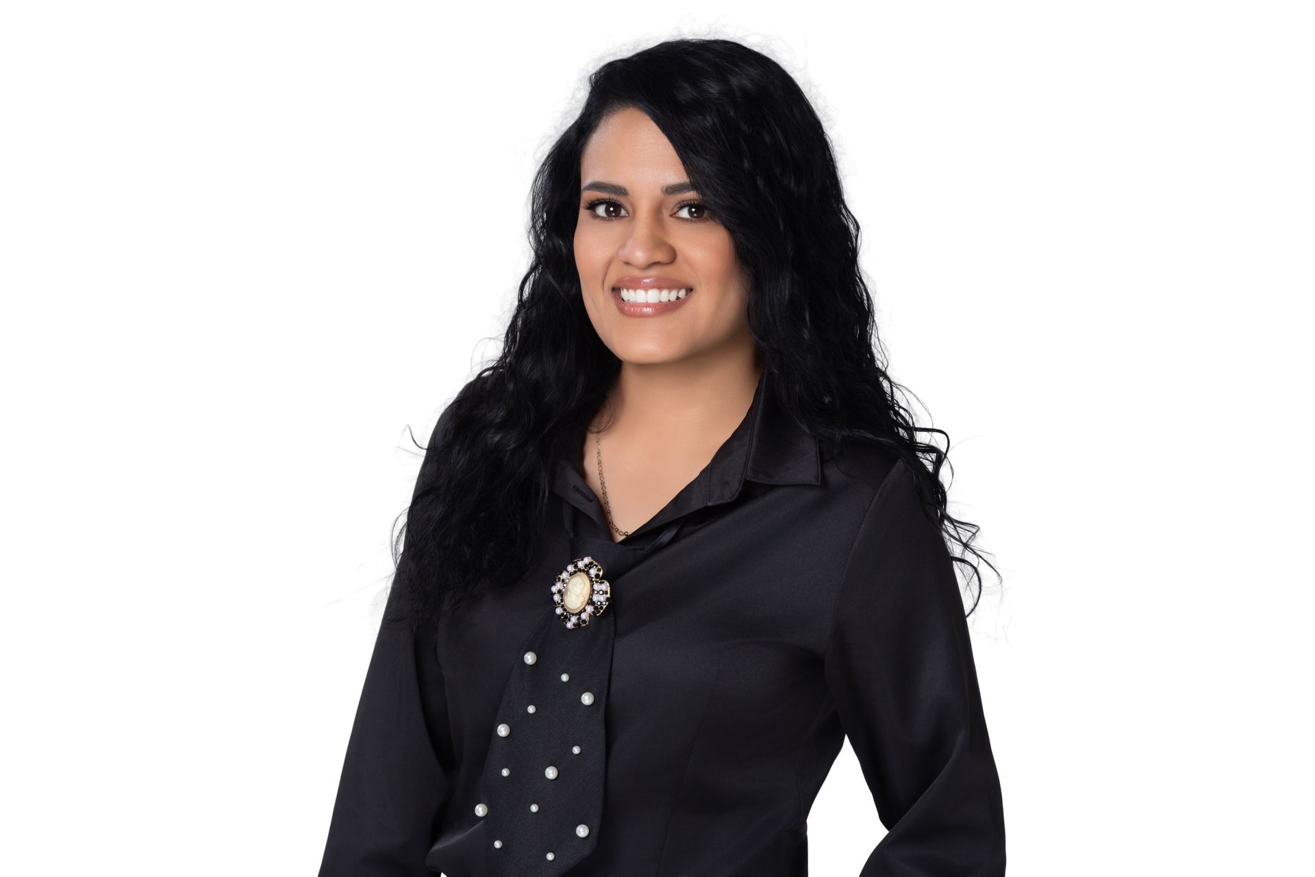 A smiling woman with long dark wavy hair wearing a black button-up shirt and a black tie with white polka dots.