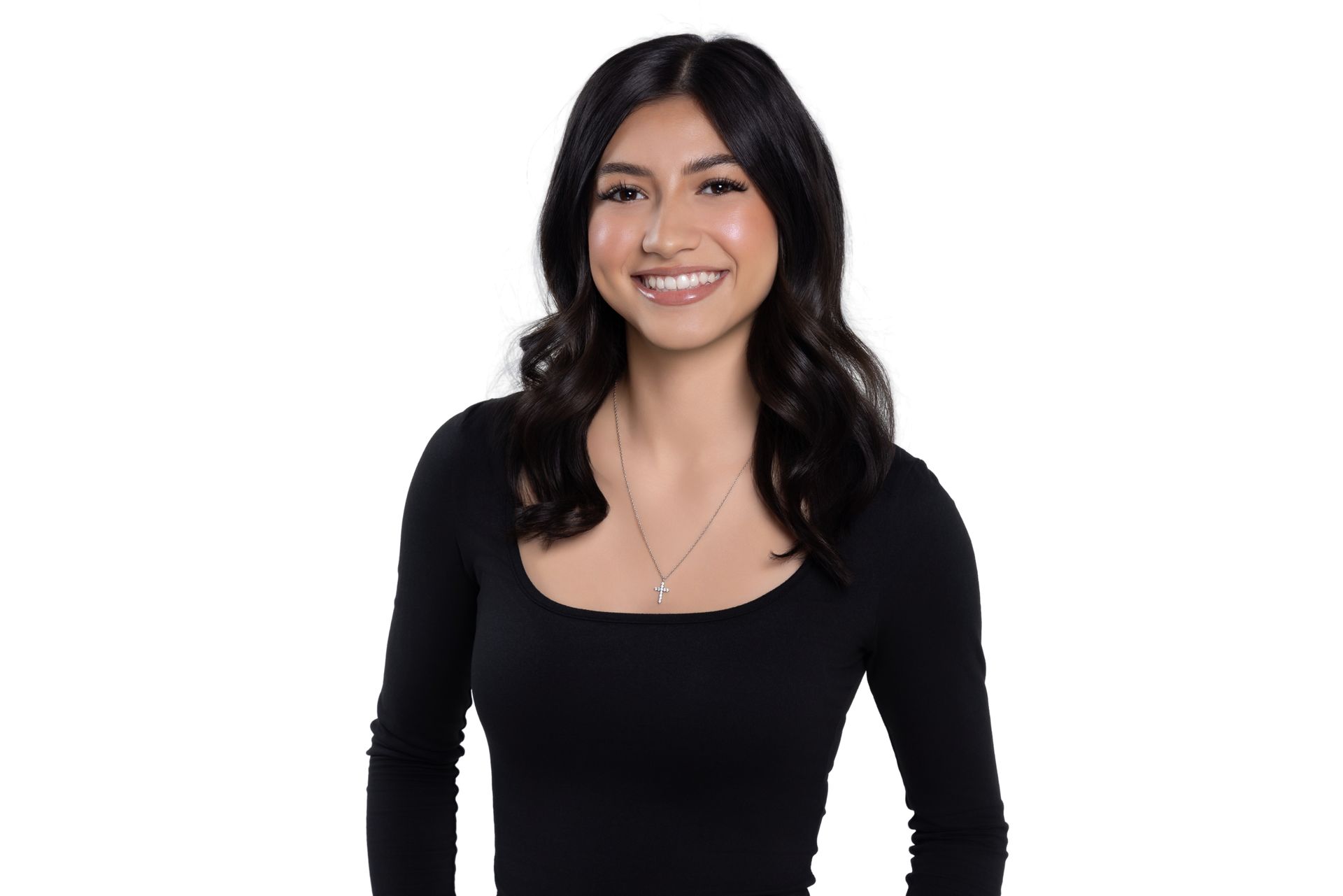 A smiling person with long dark wavy hair, wearing a black long-sleeved shirt and a delicate necklace against a white background.