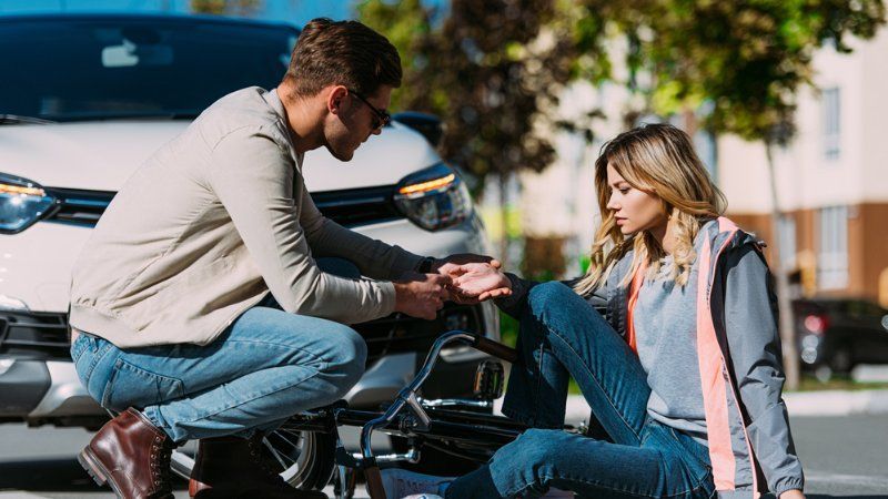 A man is kneeling on a motorcycle next to a woman who is sitting on the ground.