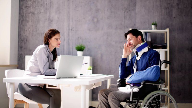A man in a wheelchair is sitting at a desk talking to a woman.