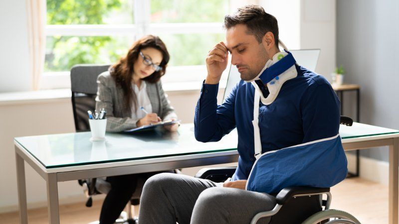 A man in a wheelchair with a broken arm is sitting at a desk with a woman.
